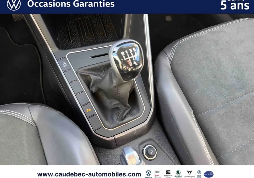 Gros plan sur la console centrale avec levier de vitesse manuel et sièges en cuir et alcantara gris d'une Volkswagen Polo noire.