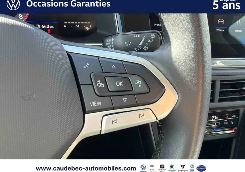 Gros plan sur les commandes au volant cuir de la Volkswagen Polo noire, avec écran digital et climatisation visible en arrière-plan.