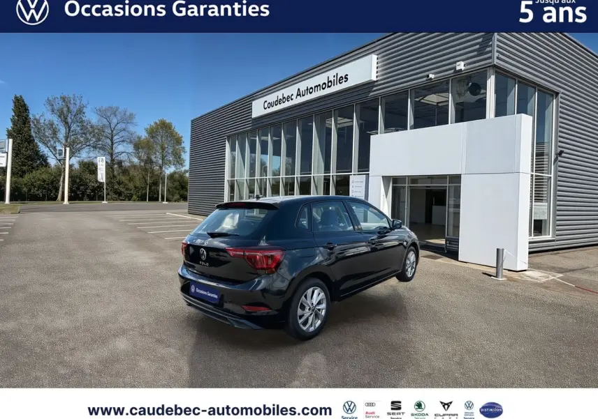 Volkswagen Polo noir intense nacré vue 3/4 arrière droit devant un bâtiment de concession Caudebec Automobiles.