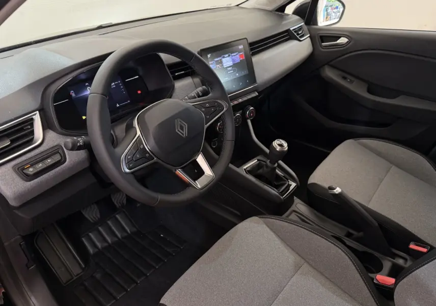 Intérieur de la Renault Clio 2025 en vue côté conducteur, tableau de bord gris avec écran tactile et volant cuir noir.