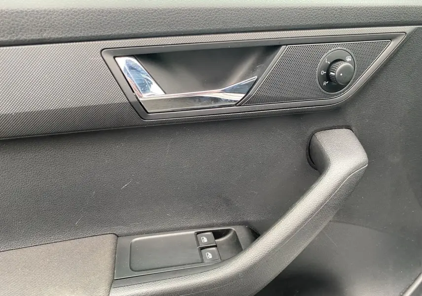 Gros plan sur la poignée intérieure côté gauche de la porte d'une Skoda Fabia gris argent, avec commandes de vitres et réglage des rétroviseurs.