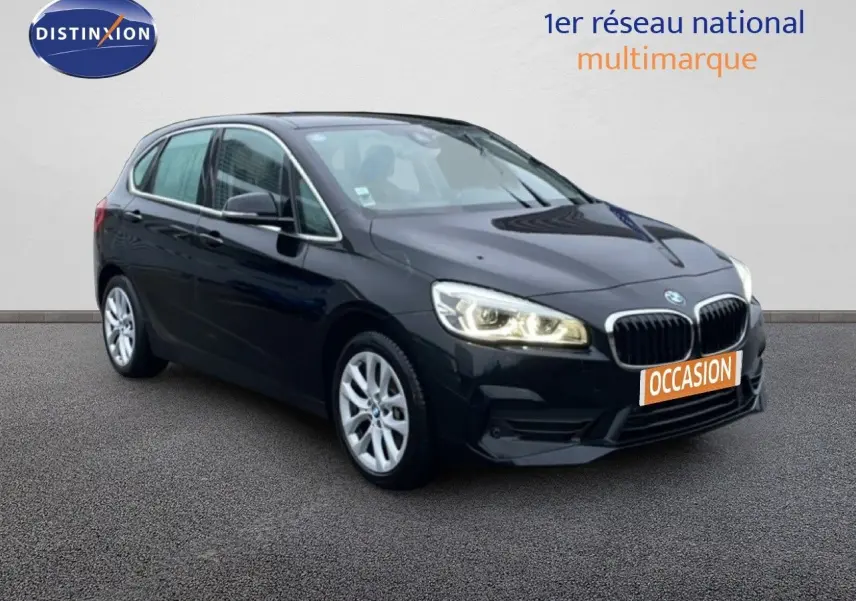 BMW Série 2 Active Tourer noir saphir métal, vue 3/4 avant droit avec phares allumés sur fond neutre.