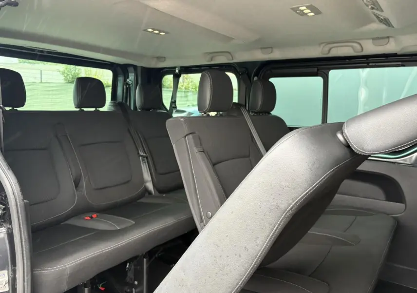 Vue intérieure côté droit du Nissan Primastar gris, montrant les sièges noirs en rangées avec appuie-têtes et ceinture de sécurité.