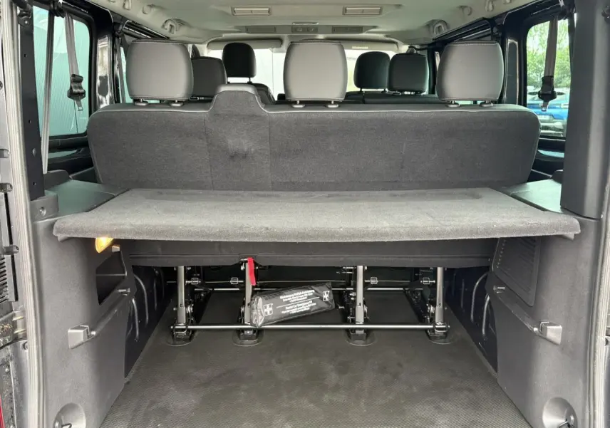 Vue arrière du coffre ouvert du Nissan Primastar gris, montrant la tablette cache-bagages et les sièges arrière.