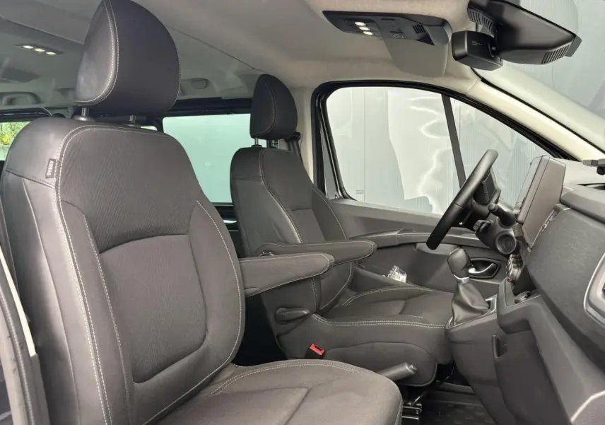 Vue intérieure côté conducteur du Nissan Primastar 2025, sièges noirs avec accoudoirs et tableau de bord moderne.