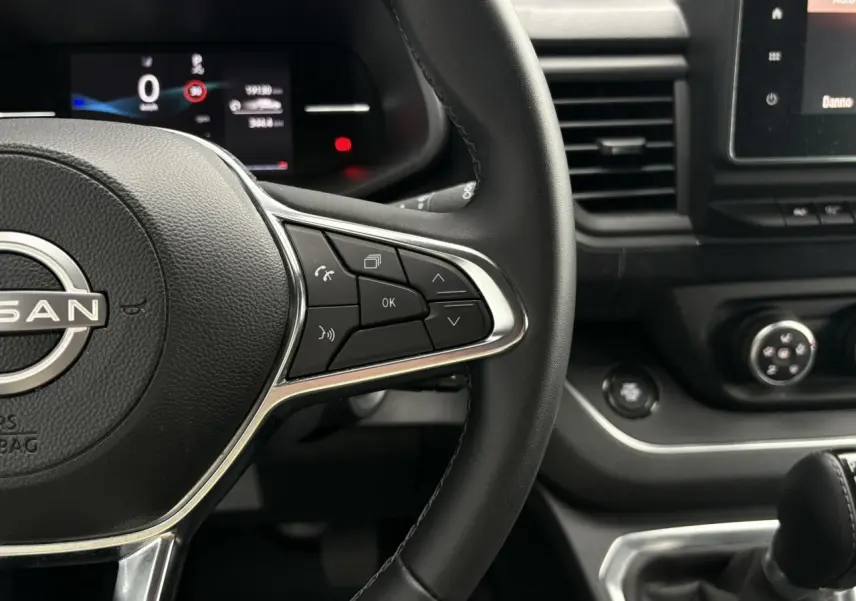 Gros plan sur le volant noir et la console centrale du Nissan Primastar 2025, avec commandes au volant et écran tactile visible.