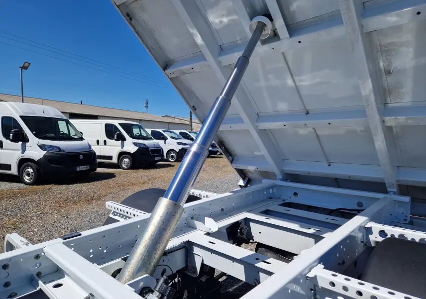 Vue rapprochée de la benne relevée blanche du Renault Master Châssis Cabine, mettant en valeur le vérin hydraulique et le châssis.