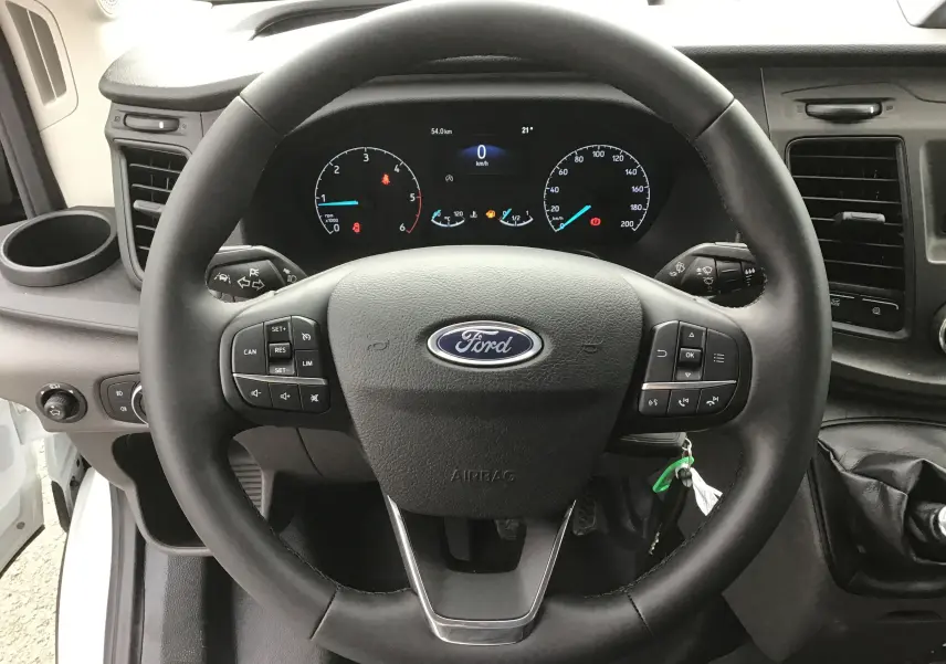 Vue rapprochée du volant Ford noir avec commandes intégrées et tableau de bord numérique du Transit Chassis Cabine blanc.
