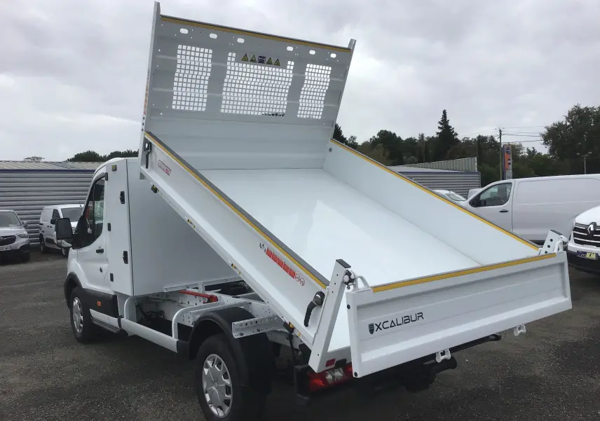 Vue 3/4 arrière droite d'un Ford Transit Chassis Cabine blanc avec benne relevée et coffre acier sur un parking.