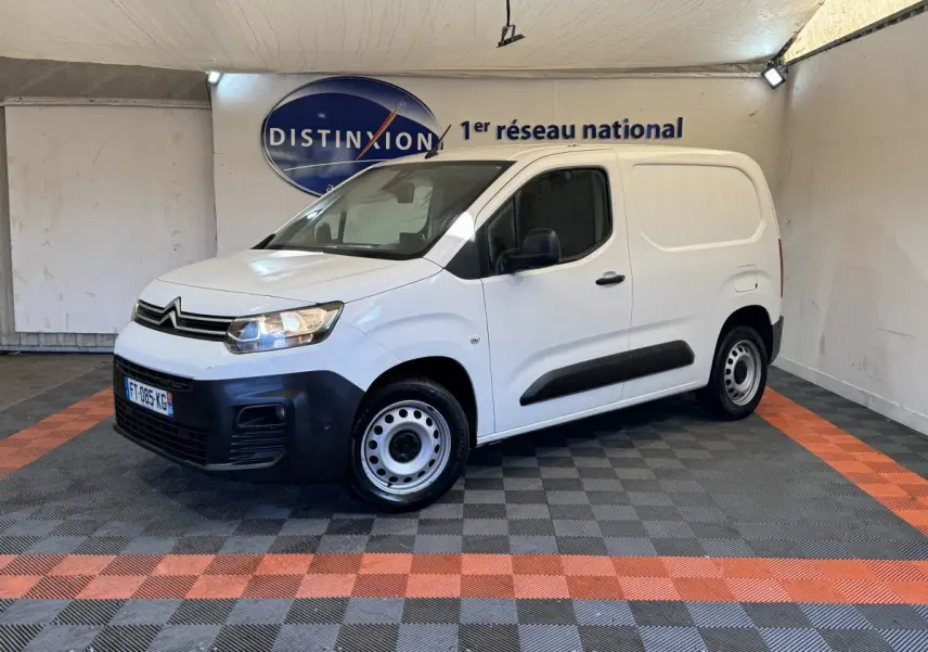 Vue 3/4 avant droite d’un utilitaire Citroën Berlingo blanc avec pare-chocs noirs et jantes acier en intérieur showroom.