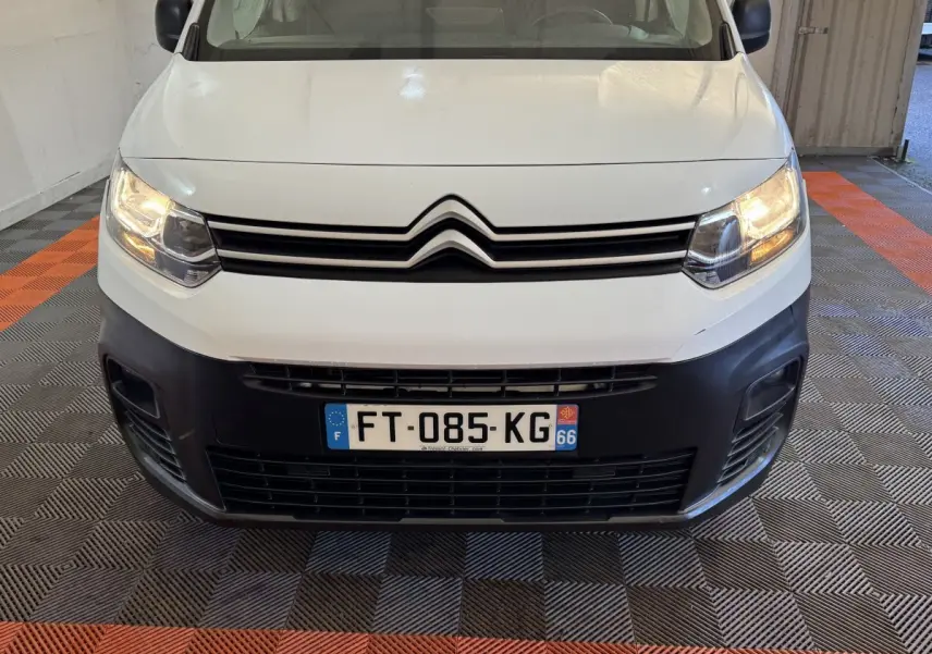 Vue avant d’un Citroën Berlingo blanc de 2020 avec phares allumés et pare-chocs noir dans un garage.