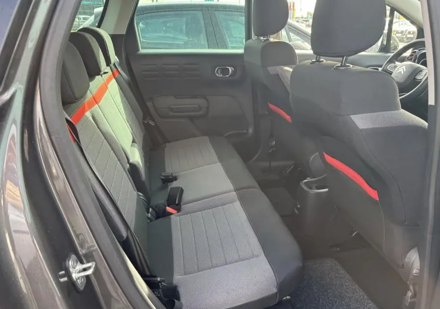 Coffre ouvert vu de l'arrière d'une Citroën C3 Aircross gris platinium avec intérieur noir et banquette rabattue partiellement.