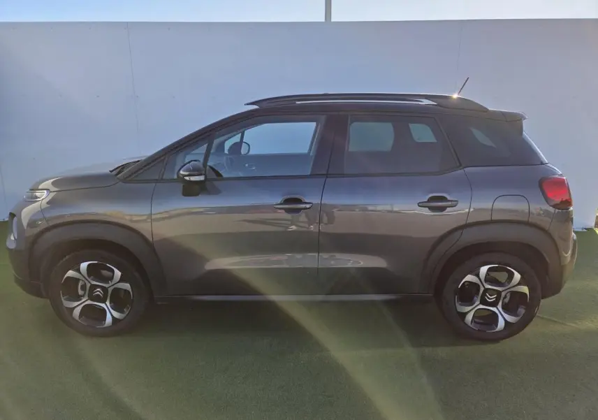 Vue de face d'un Citroën C3 Aircross gris platinium avec toit noir perlé et barres de toit argentées sur fond urbain.