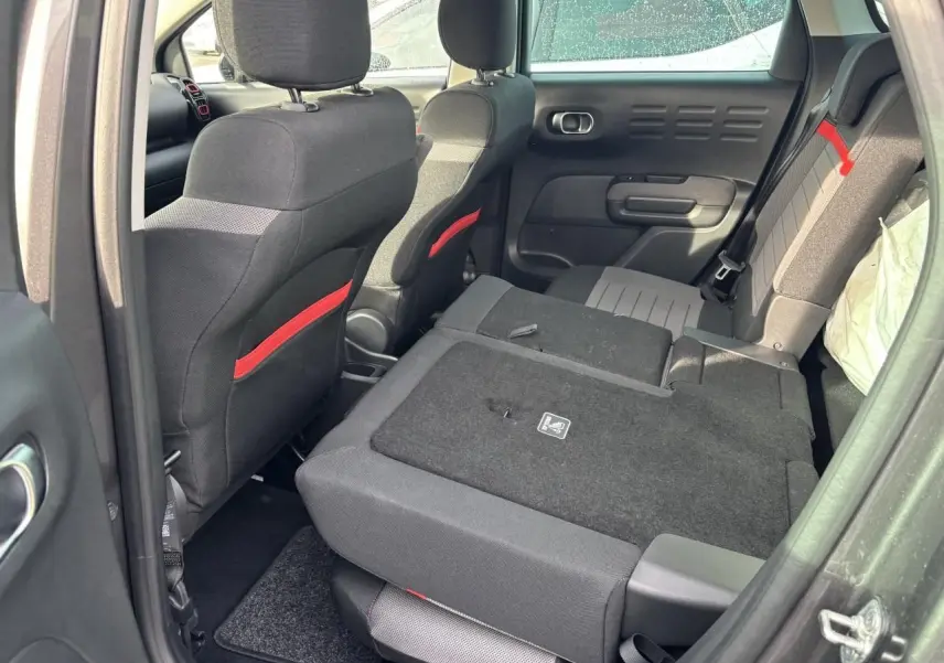 Vue intérieure arrière droite du Citroën C3 Aircross gris, banquette arrière rabattue avec détails rouges sur sièges avant.