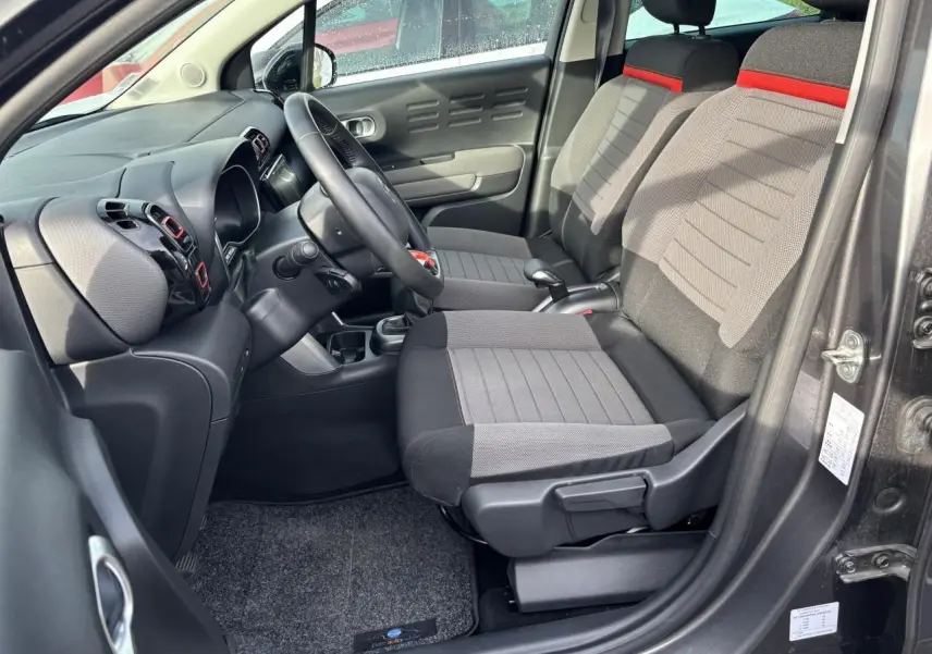 Vue intérieure côté conducteur du Citroën C3 Aircross 2021, sièges tissu gris avec bande rouge et tableau de bord noir.