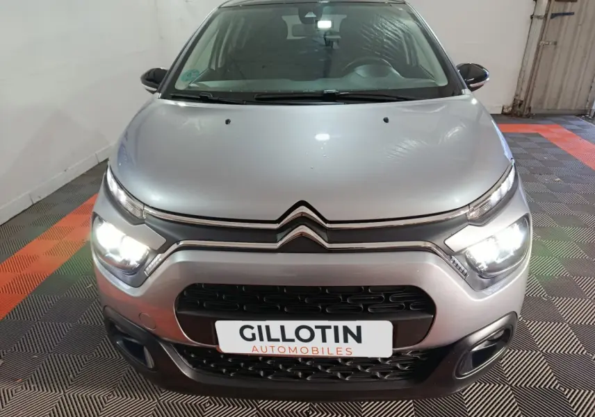 Vue frontale d'une Citroën C3 gris foncé avec phares LED allumés dans un garage au sol carrelé noir et orange.