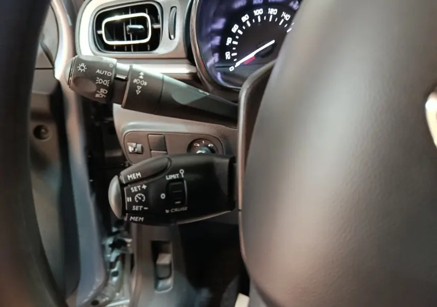 Gros plan sur la commande de régulateur de vitesse à gauche du volant d'une Citroën C3 gris foncé 2024.