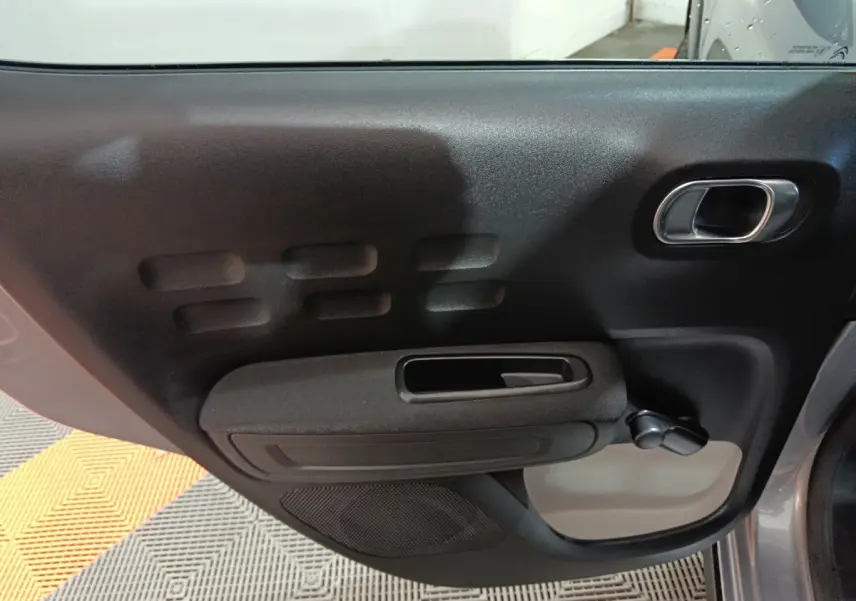 Vue rapprochée de la porte côté gauche intérieure d'une Citroën C3 gris foncé avec poignée chromée et manivelle de vitre.