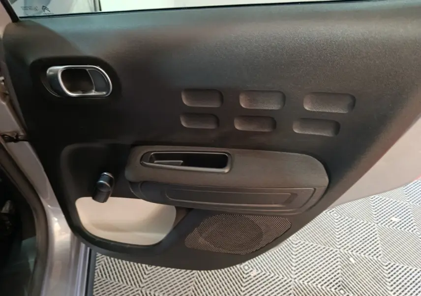 Vue rapprochée de la porte avant gauche intérieure de la Citroën C3 gris foncé avec poignée et haut-parleur intégrés.