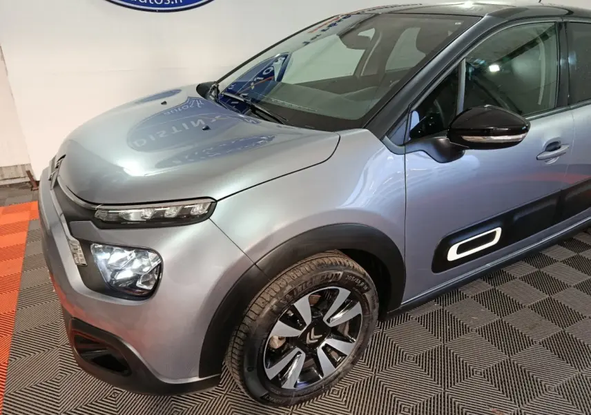 Vue 3/4 avant droit d'une Citroën C3 gris foncé avec phares LED et protections latérales blanches distinctives.