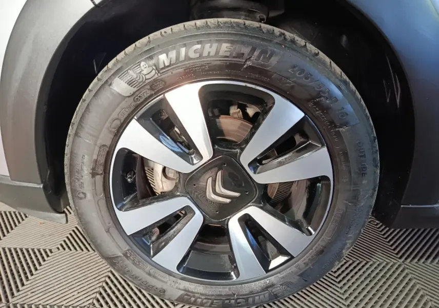 Gros plan sur la roue avant droite d'une Citroën C3 gris foncé, mettant en valeur la jante bicolore et le logo Citroën central.