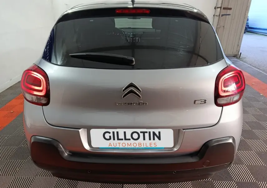 Vue arrière d'une Citroën C3 gris clair avec feux arrière allumés et pare-chocs noir dans un garage.