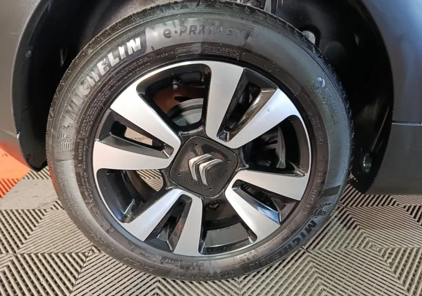 Gros plan sur la jante alliage bicolore avec logo Citroën, montée sur un pneu Michelin d'une C3 gris foncé 2024.