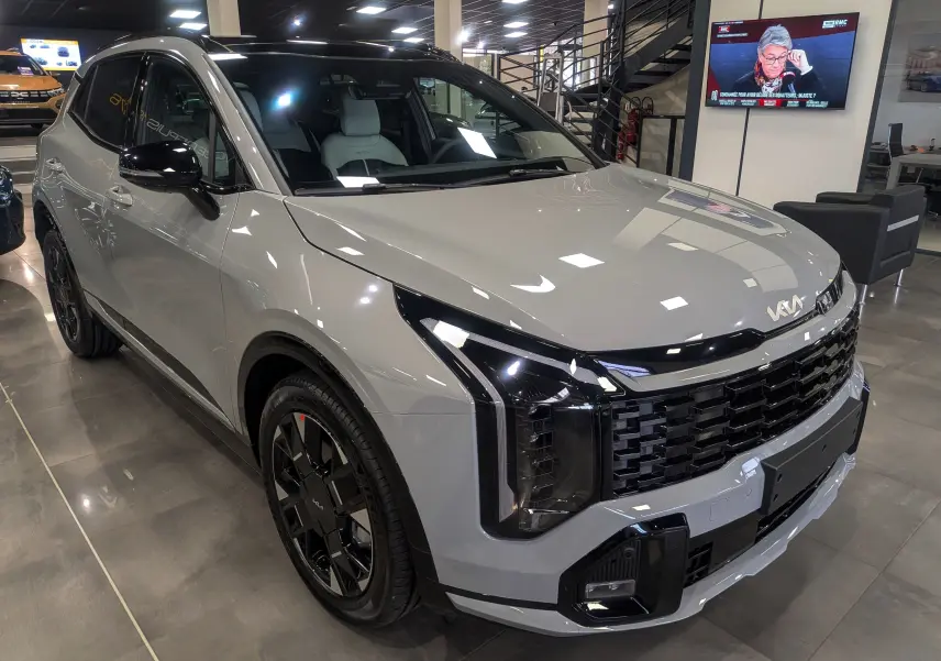 Kia Sportage 2025 gris céramique avec toit noir, vue 3/4 avant droit, calandre et phares modernes en showroom.