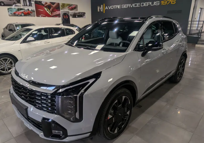 KIA SPORTAGE gris céramique avec toit noir, vue 3/4 avant droit en intérieur de showroom.