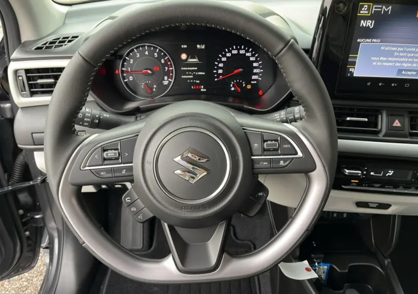 Vue intérieure centrée sur le volant cuir multifonctions d'une Suzuki Swift gris minéral avec tableau de bord et écran tactile.