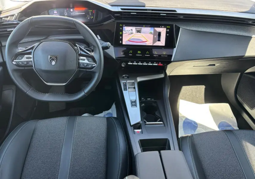 Vue intérieure avant de la Peugeot 408 Hybrid noire, avec volant compact, écran tactile central et cockpit numérique.