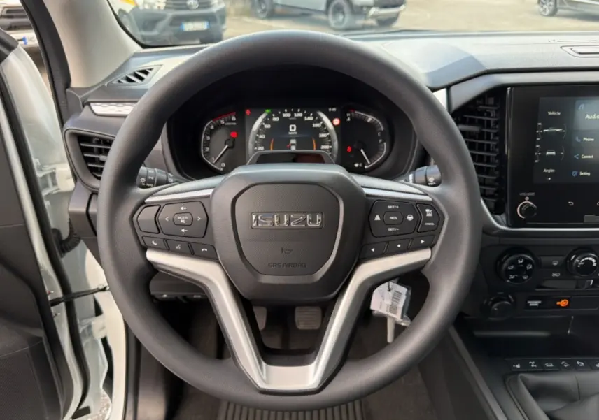 Vue rapprochée du volant multifonctions noir de l'Isuzu D-MAX 2026 avec tableau de bord et écran tactile visible.