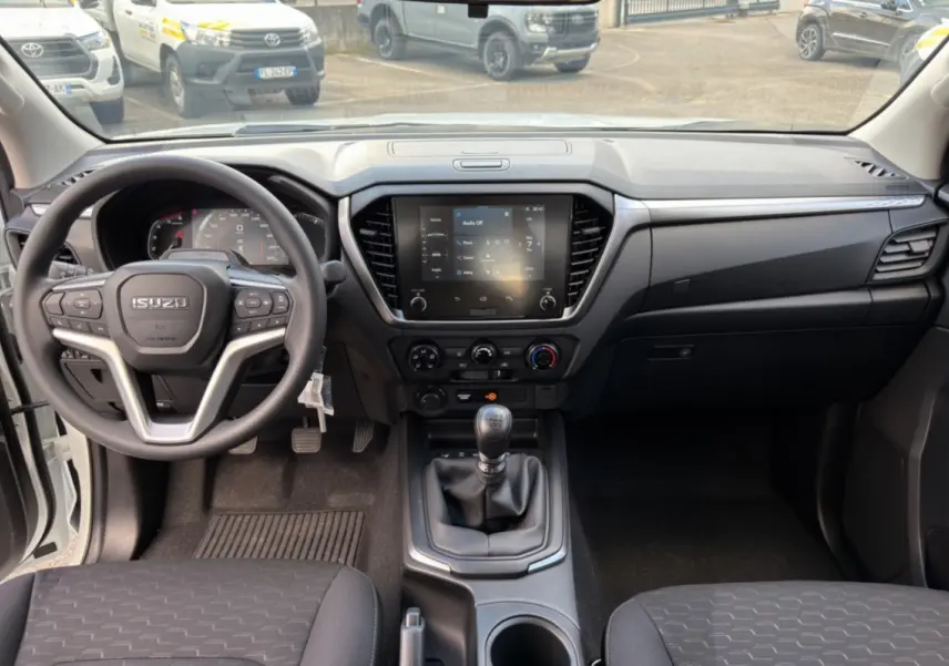 Intérieur de l'Isuzu D-MAX 2026 vue de face, tableau de bord noir avec écran tactile et boîte manuelle.