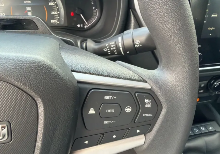 Gros plan sur les commandes au volant du Isuzu D-MAX 2026, finition Splash White, avec tableau de bord partiellement visible.