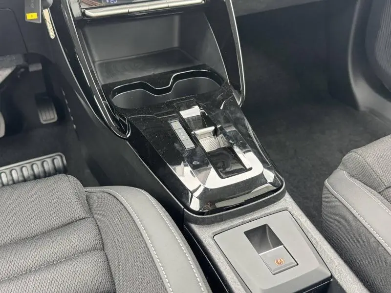 Vue rapprochée de la console centrale noire brillante avec levier de boîte auto et frein à main électrique, sièges gris tissu.