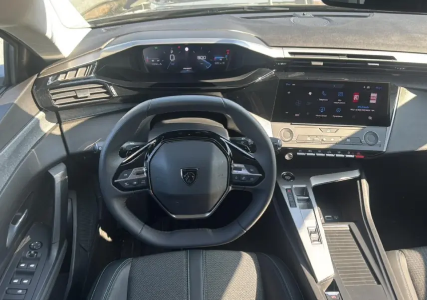 Vue intérieure frontale du poste de conduite gris de la Peugeot 308 2025 avec volant multifonction et écran tactile central.