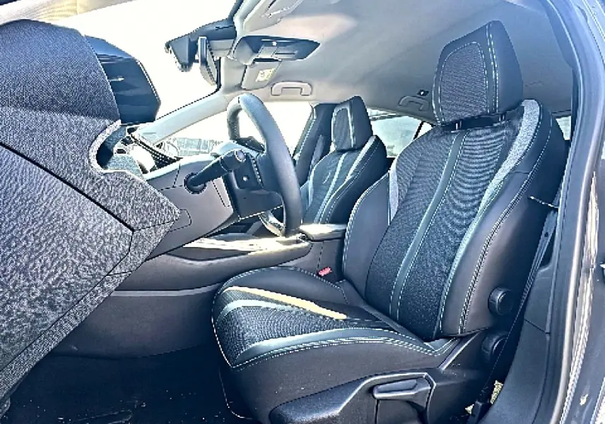 Vue intérieure côté conducteur de la Peugeot 308 2025, sièges tissu noir avec surpiqûres contrastées et volant multifonction.