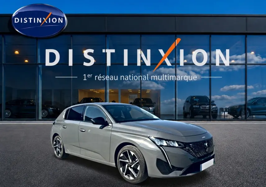 Peugeot 308 gris en 3/4 avant droit, avec jantes alu et calandre distinctive, devant une vitrine Distinxion.
