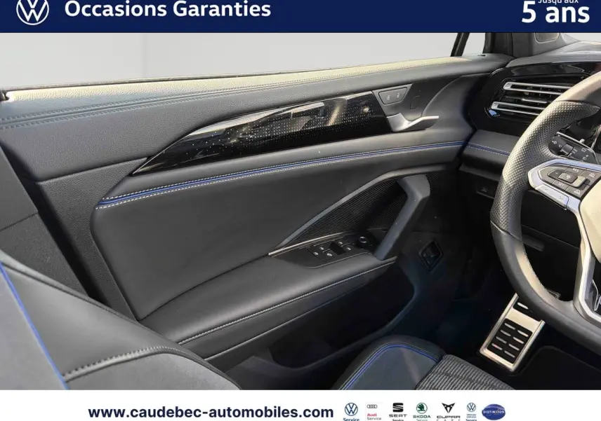 Vue intérieure côté conducteur du Volkswagen Tiguan 2025, cuir noir avec surpiqûres bleues et volant sport partiel visible.