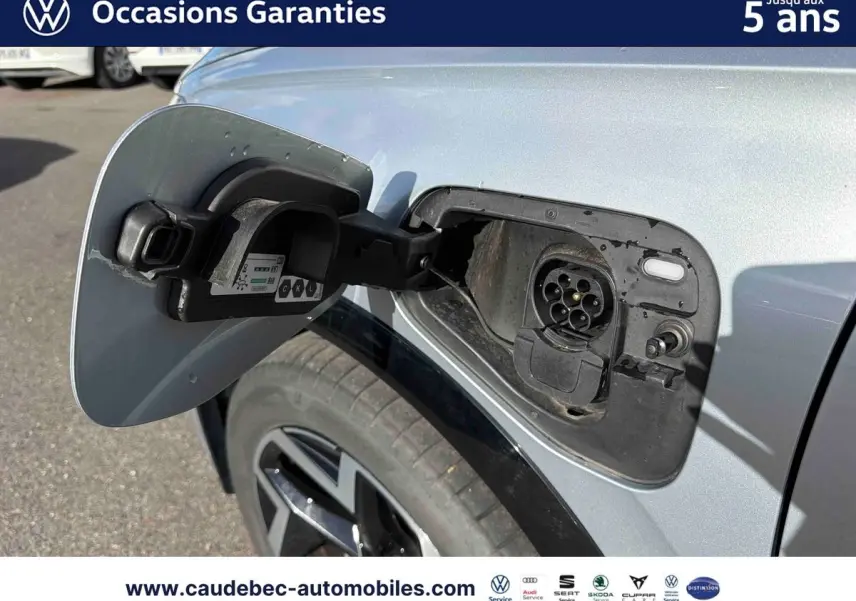 Gros plan sur la trappe de recharge avant gauche du Volkswagen Tiguan eHybrid argent Dolomite, roue et carrosserie visibles.