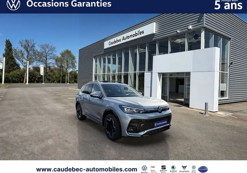 Volkswagen Tiguan 1.5 eHybrid argent Dolomite en 3/4 avant droit devant un showroom Caudebec Automobiles.