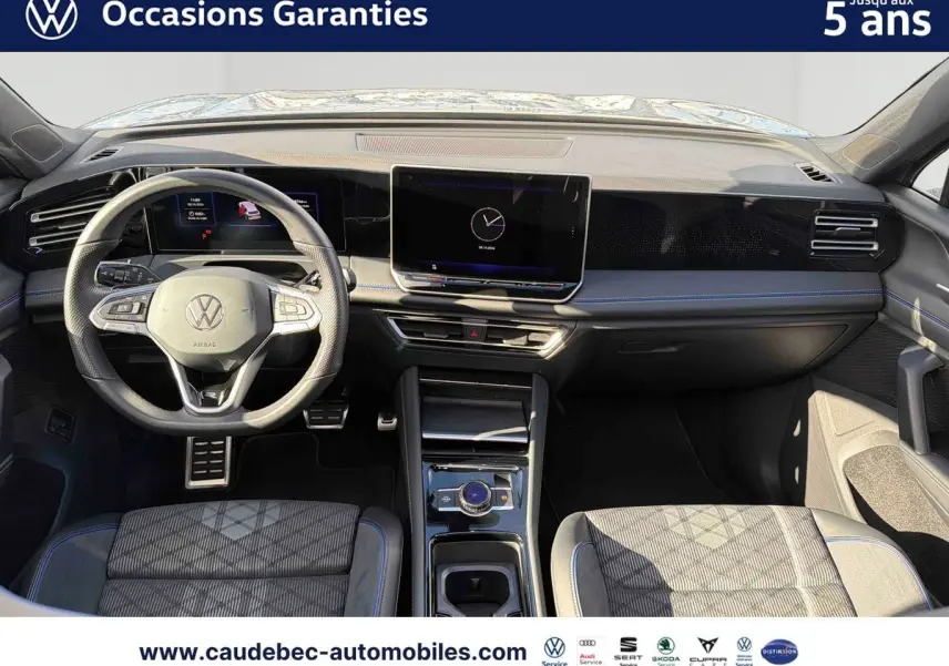 Vue intérieure avant du Volkswagen Tiguan 2025, tableau de bord noir avec écran tactile central et volant multifonction.