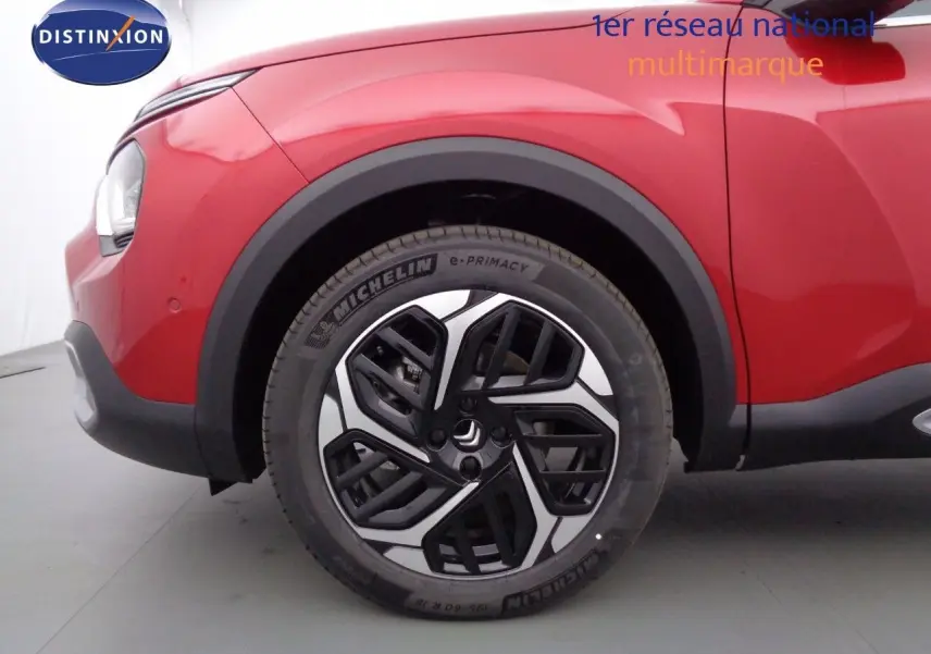 Gros plan sur la roue avant droite d'une Citroën C4 X rouge Elixir Métal avec jante noire et argentée design moderne.