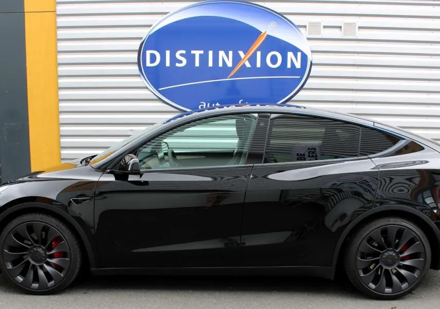Profil côté gauche d'une Tesla Model Y Performance noire métal, avec jantes noires et étriers de frein rouges visibles.