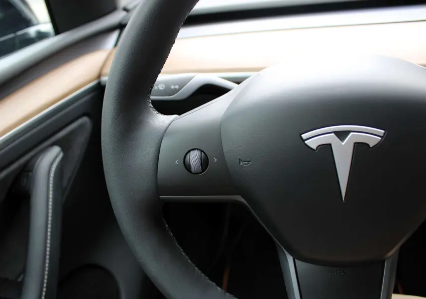 Gros plan sur le volant noir de la Tesla Model Y 2024 avec logo argenté et tableau de bord en bois clair.