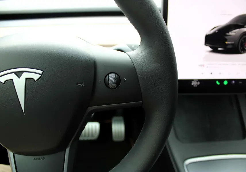 Gros plan sur le volant noir de la Tesla Model Y 2024 avec écran tactile affichant une image du véhicule noir métal.