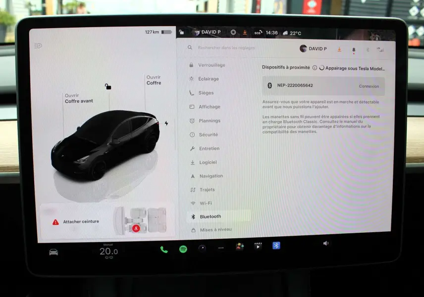 Écran tactile intérieur montrant la Tesla Model Y noire métal en vue 3/4 avant avec options d'ouverture des coffres.
