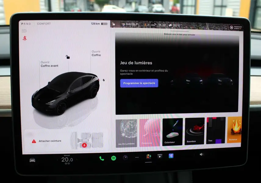 Écran tactile montrant une Tesla Model Y noire métal en vue 3/4 avant avec options d'ouverture des coffres.