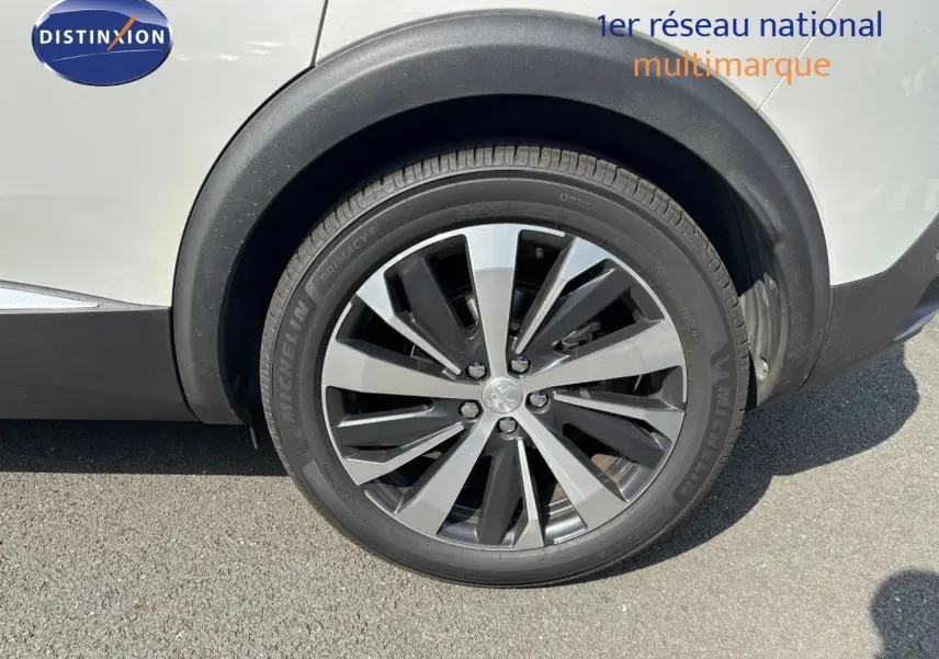 Gros plan sur la roue avant droite d'un Peugeot 3008 blanc nacré avec jante alliage bicolore moderne.