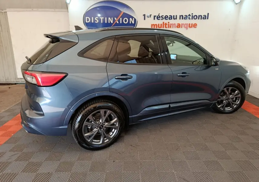 Vue latérale côté gauche d'un Ford Kuga bleu 2024 avec jantes alliage et vitres teintées en intérieur showroom.